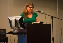 Image displays UMBC professor Dr. Bambi Chapin at a computer speaking into the mic with a green shirt on.