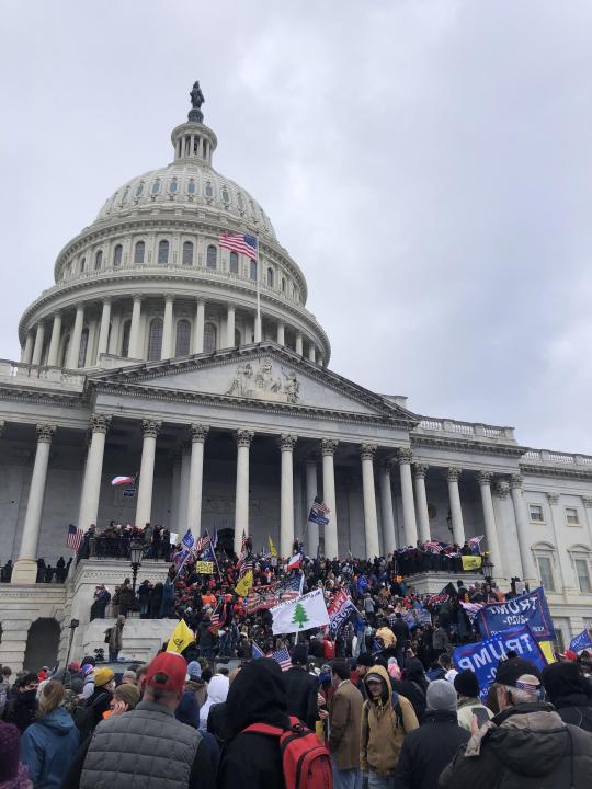 This is a photo of the Capitol building during the 2021 Insurrection. There is a group of pro-Trump rioters holding signs, ready to break into the Capitol building.